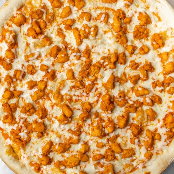 A close-up overhead view of a Farmers Pizza buffalo chicken pizza with white sauce and cheese.